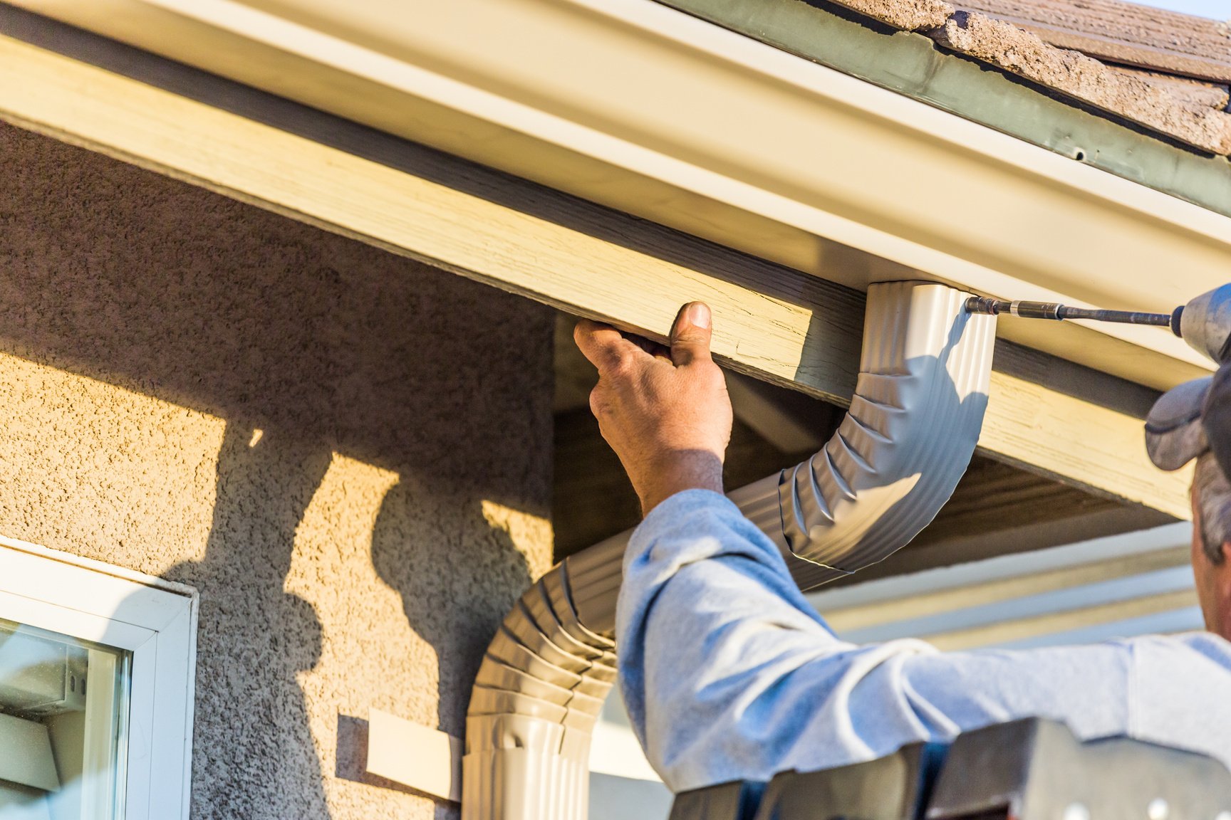 Worker Attaching Aluminum Rain Gutter and Down Spout to Fascia